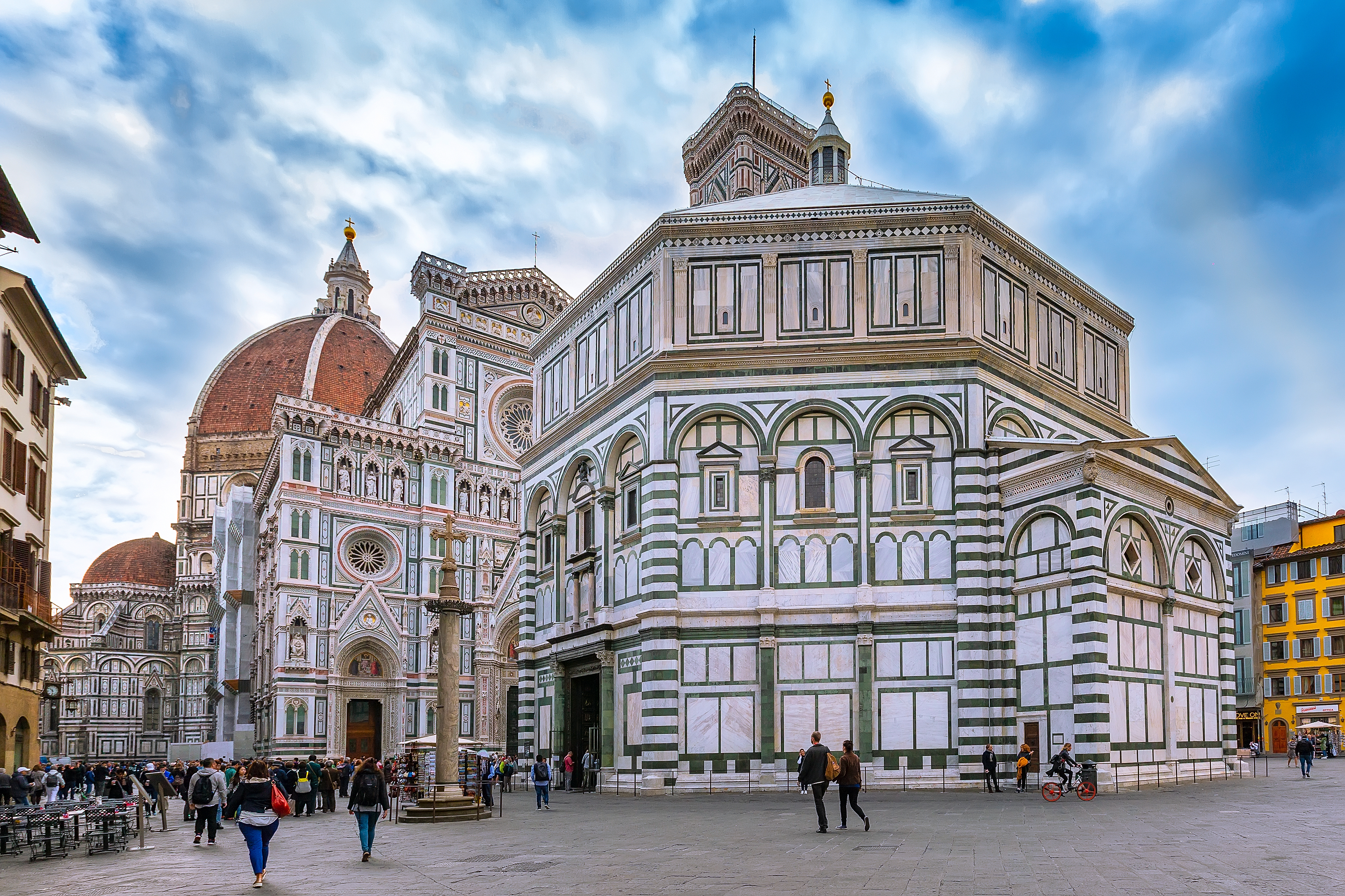 People on the square near historical medieval Duomo Santa Maria Del Fiore and Baptistery in old town, cloudy blue sky